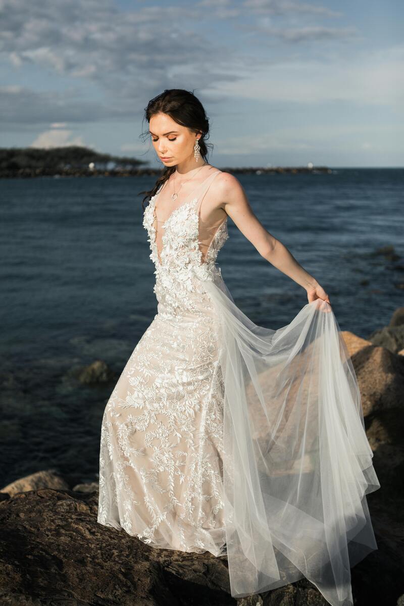 Nachdenkliche Frau im weißen Spitzenkleid am Meer, hält Schleierstoff