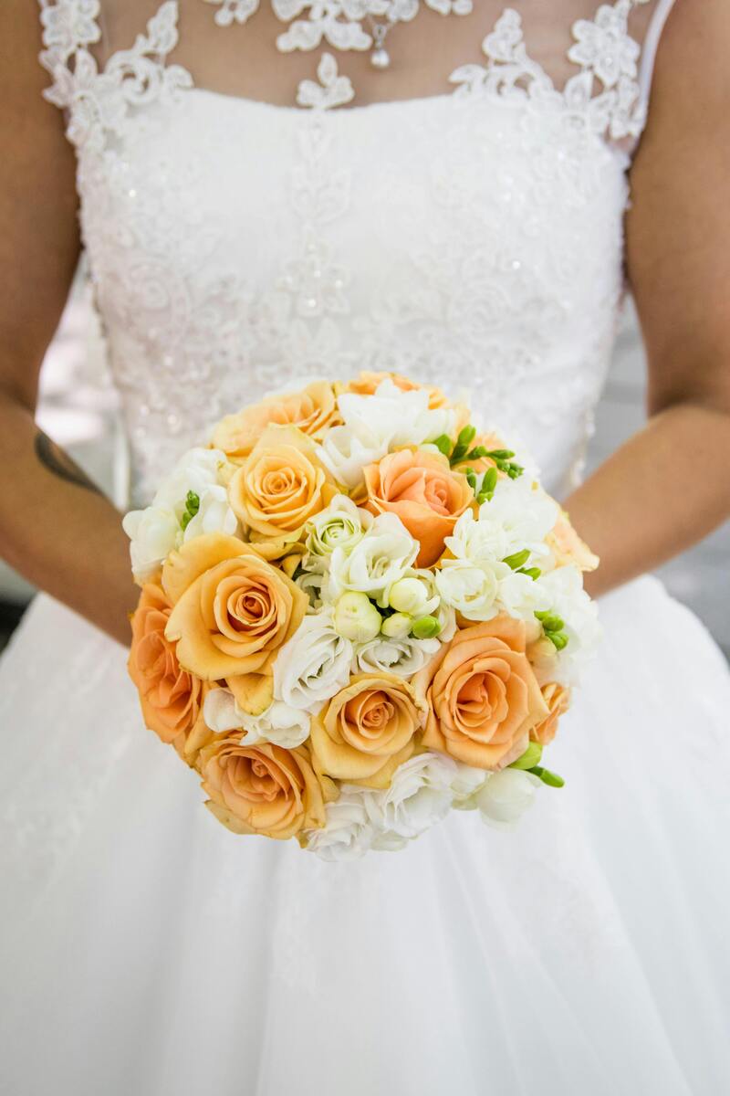 Braut ohne Gesicht hält lächelnd orange weiße Rosen, weißes Kleid mit Spitze